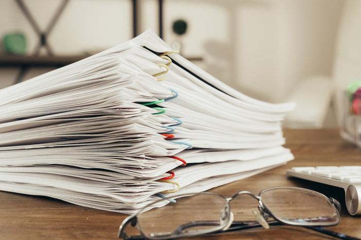 Stack of papers with colorful paperclips on a desk next to glasses.